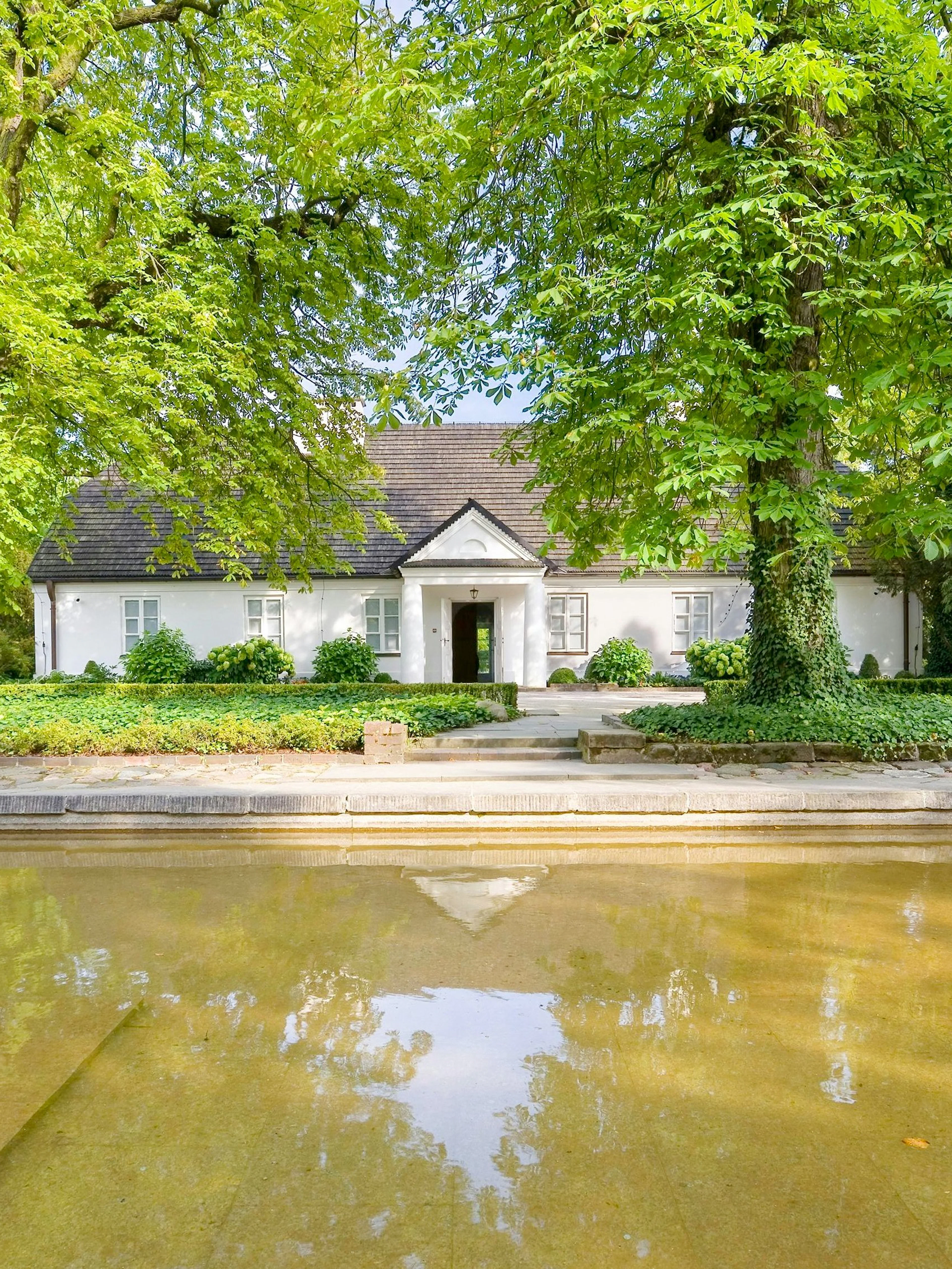 Birthplace of Frederick Chopin in Żelazowa Wola, surrounded by lush greenery and a reflecting pond.