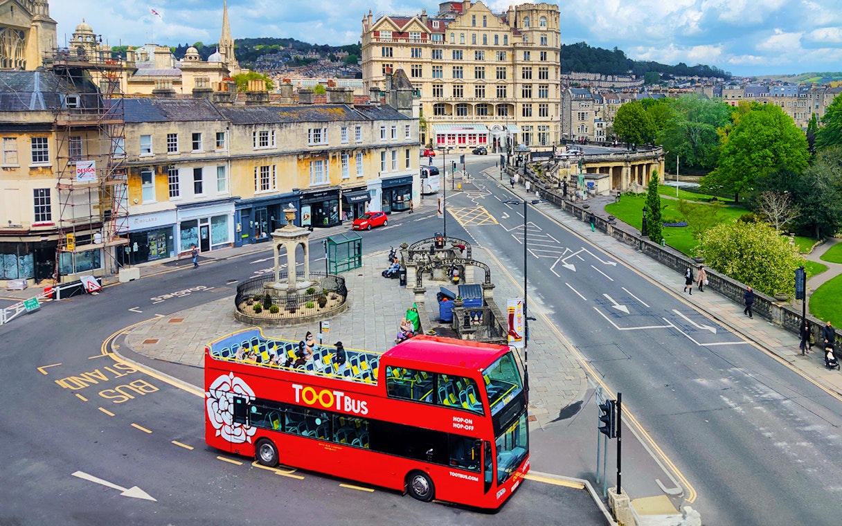 Red Tootbus on Bath street during hop-on hop-off tour, passing historic buildings.