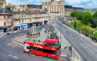 Red Tootbus on Bath street during hop-on hop-off tour, passing historic buildings.