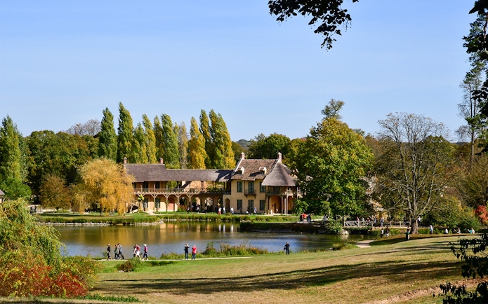 Queen's Hamlet in Versailles with rustic buildings by a pond surrounded by trees.