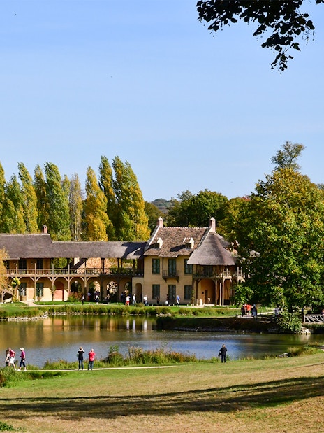 Queen's Hamlet in Versailles with rustic buildings by a pond surrounded by trees.