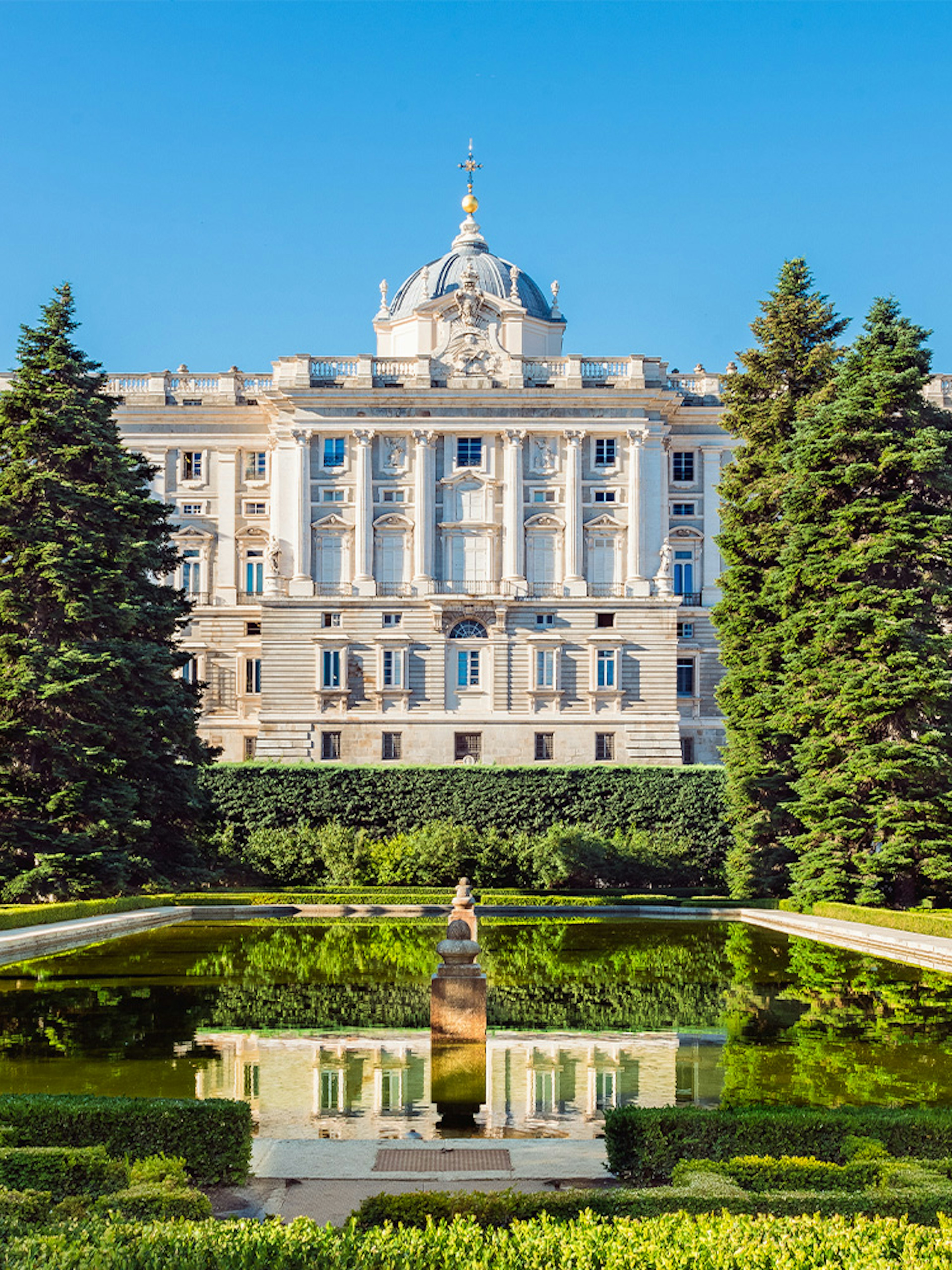 Royal Palace of Madrid exterior with garden and reflecting pool.