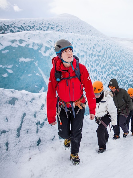 Hikers trekking on Falljökull glacier in Iceland, wearing helmets and winter gear.