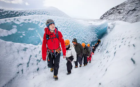 Hikers trekking on Falljökull glacier in Iceland, wearing helmets and winter gear.