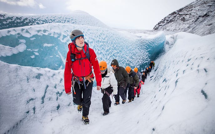 Hikers trekking on Falljökull glacier in Iceland, wearing helmets and winter gear.