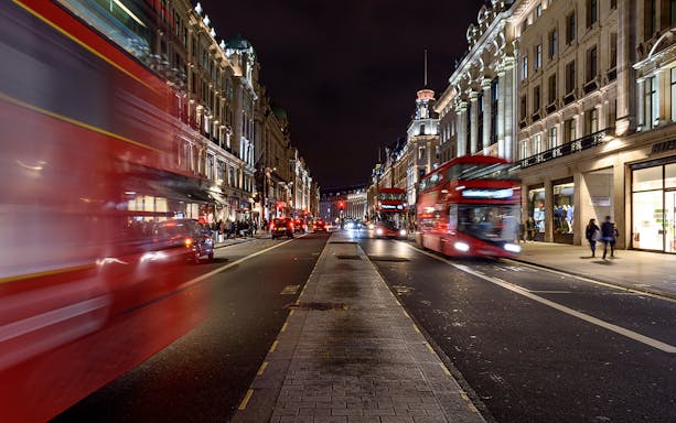 Red double-decker buses on a busy London street at night during the Big Bus Panoramic Evening Tour.