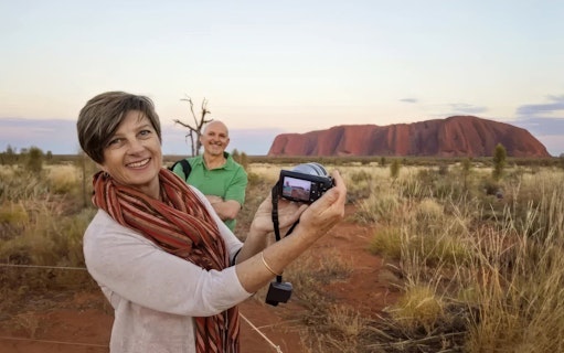 Tourists photographing Uluru at sunset during a small group tour from Alice Springs.