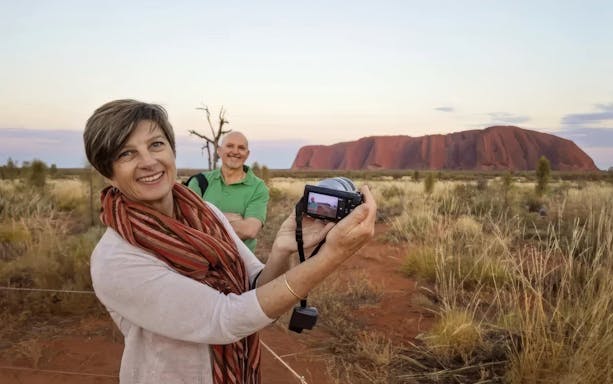 Tourists photographing Uluru at sunset during a small group tour from Alice Springs.
