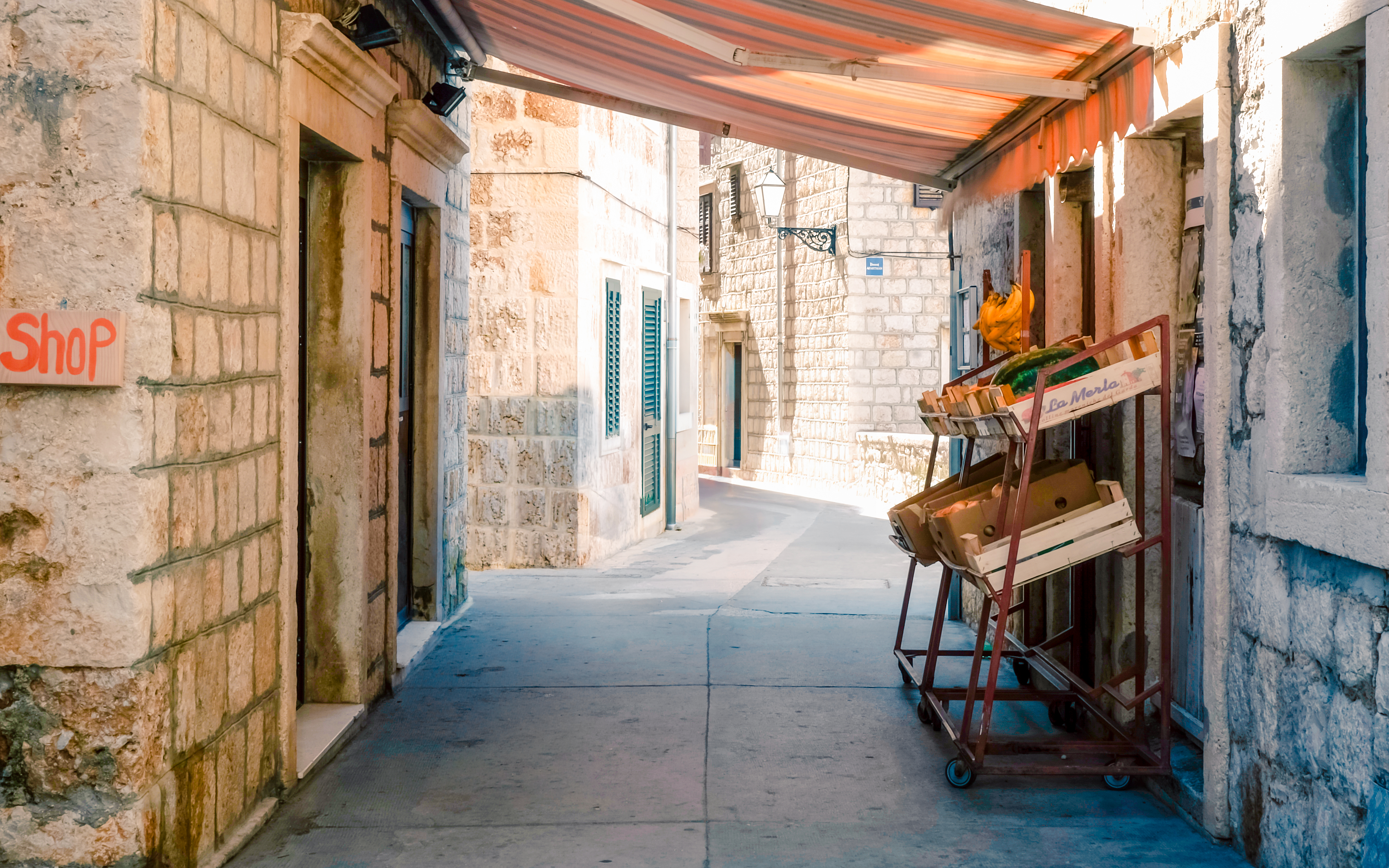 Narrow alley with stone buildings and a fruit cart, Komiza, Vis Island, Croatia.