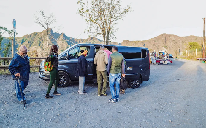 Group boarding a van with a professional driver in a mountainous area.