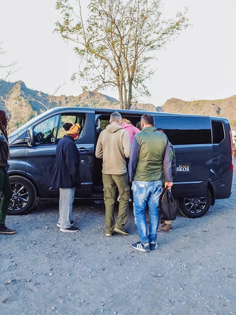 Group boarding a van with a professional driver in a mountainous area.