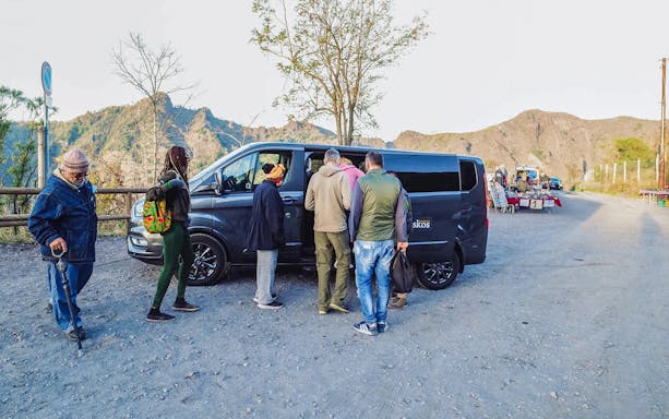 Group boarding a van with a professional driver in a mountainous area.