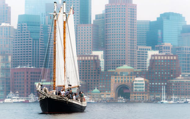Schooner Liberty Star sailing in Boston Harbor with city skyline in background.