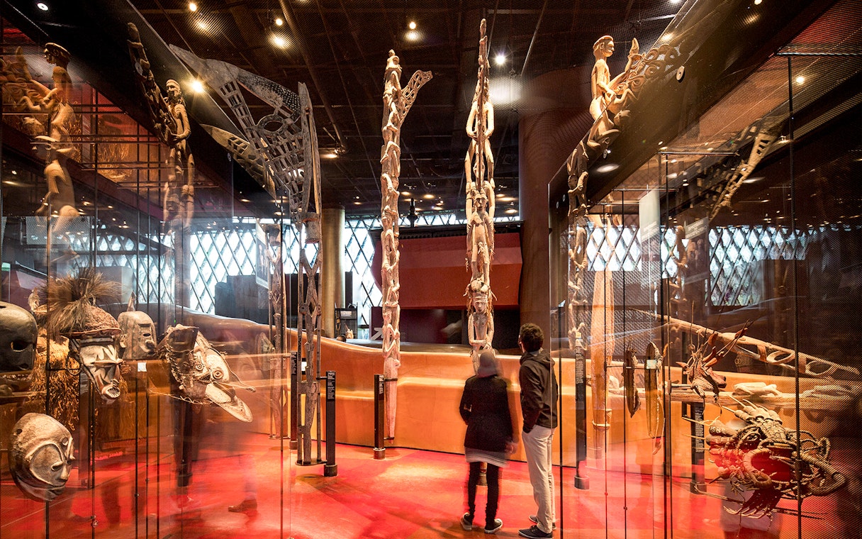 Musee du Quai Branly interior with visitors viewing tribal masks and sculptures.