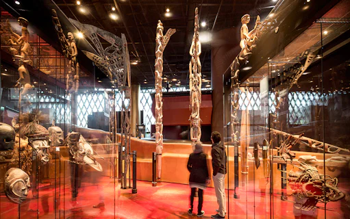 Musee du Quai Branly interior with visitors viewing tribal masks and sculptures.