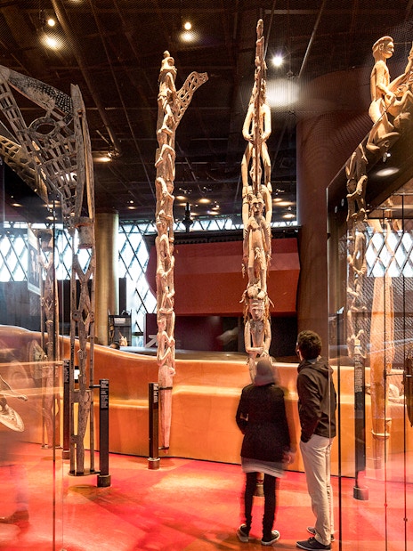 Musee du Quai Branly interior with visitors viewing tribal masks and sculptures.