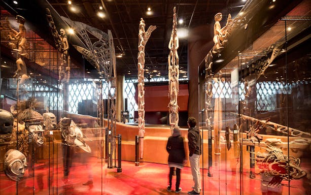 Musee du Quai Branly interior with visitors viewing tribal masks and sculptures.