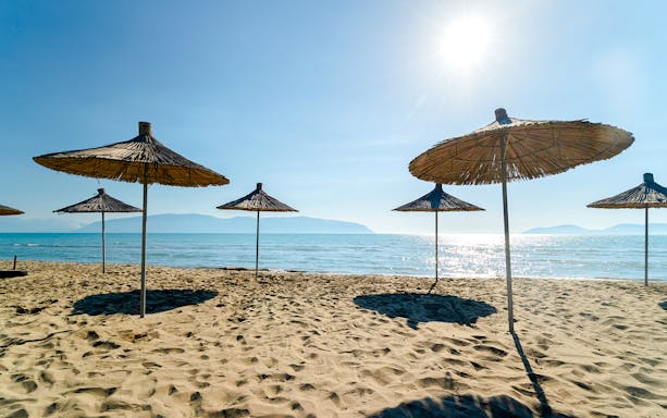 Sunlit beach with straw umbrellas on Karaburun Peninsula, Albania.