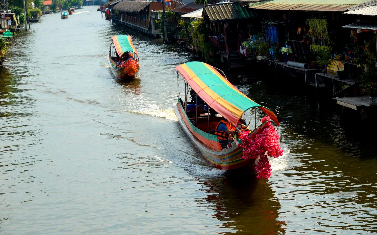 Longtail boats navigating Bangkok canal with vibrant decorations.