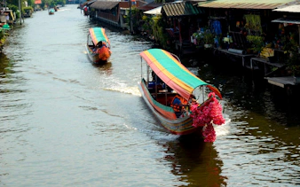 Longtail boats navigating Bangkok canal with vibrant decorations.