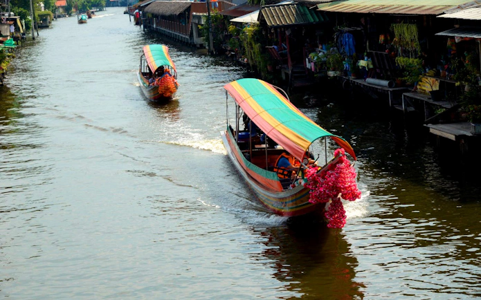Longtail boats navigating Bangkok canal with vibrant decorations.