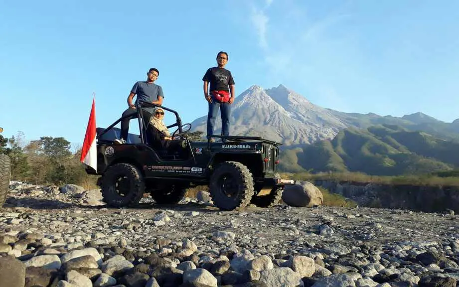 Jeep tour at Mount Merapi with three people, rocky terrain, and mountain view in the background.