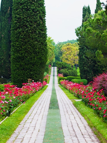 Pathway lined with vibrant flowers and tall trees at Sigurta Park, Italy.