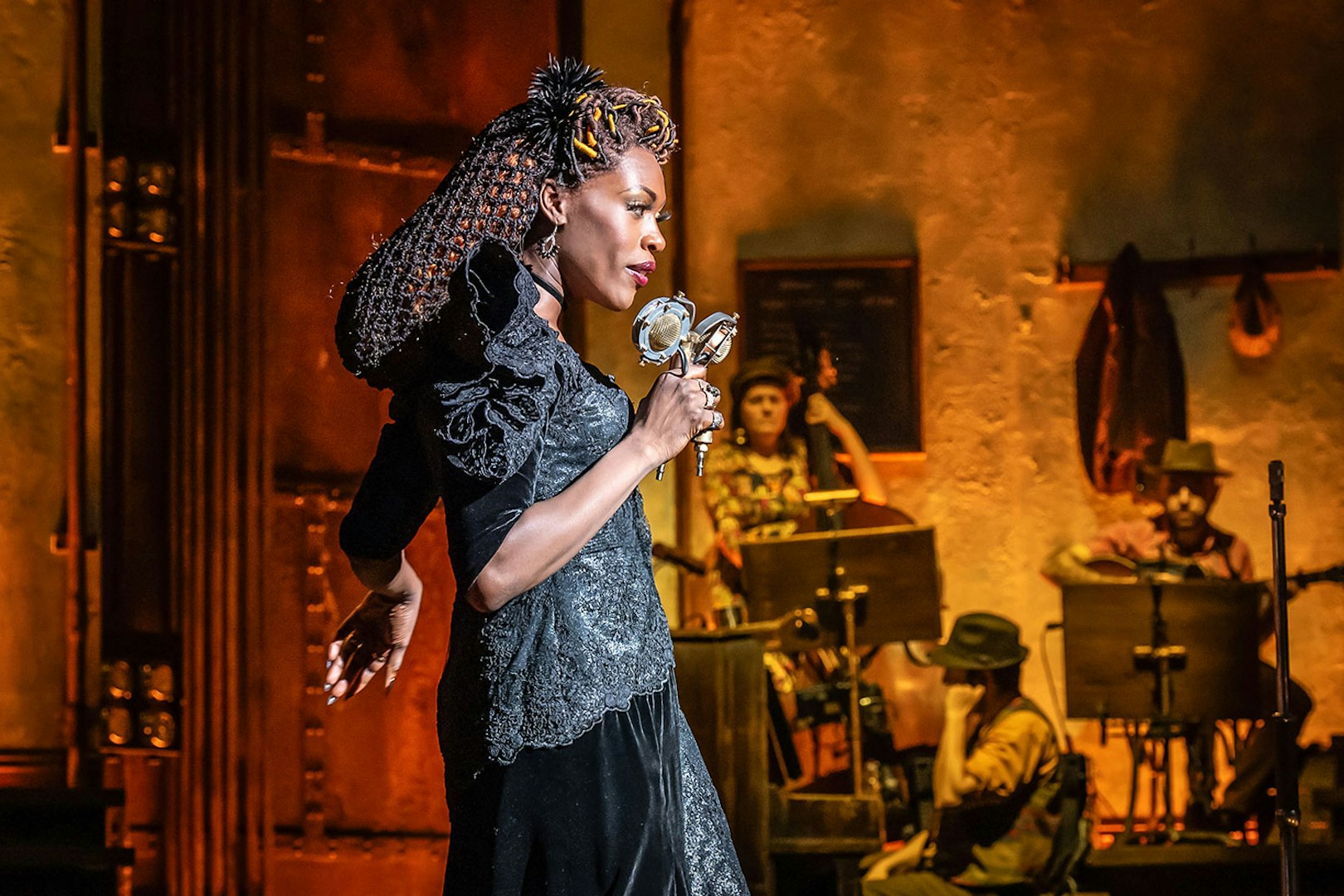 Performer singing on stage during Hadestown musical with band in background.