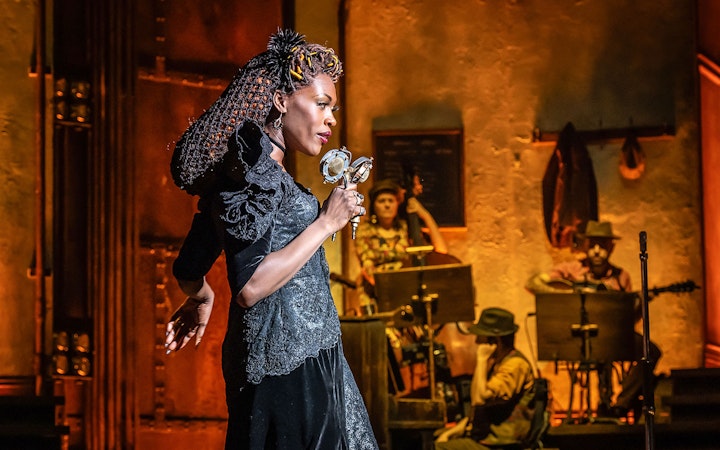 Performer singing on stage during Hadestown musical with band in background.