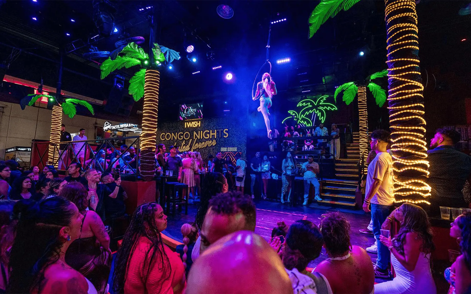 Crowd enjoying a vibrant night show at Coco Bongo Congo Bar with acrobatics and neon lights.
