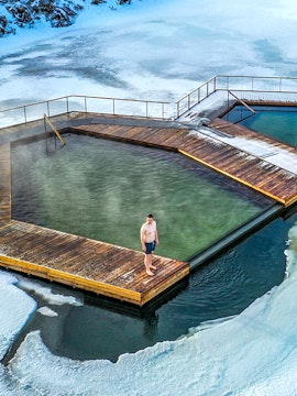 Guest standing on wooden deck at Vok Baths, surrounded by icy water in Iceland.