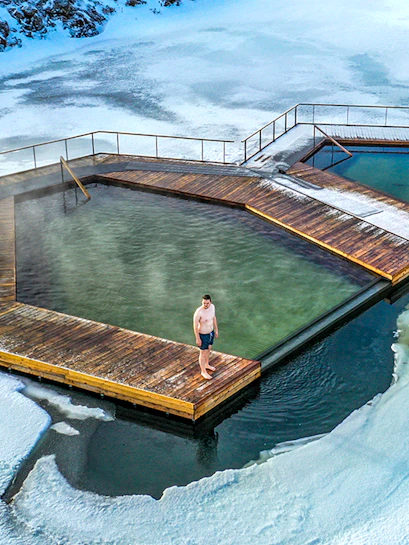 Guest standing on wooden deck at Vok Baths, surrounded by icy water in Iceland.