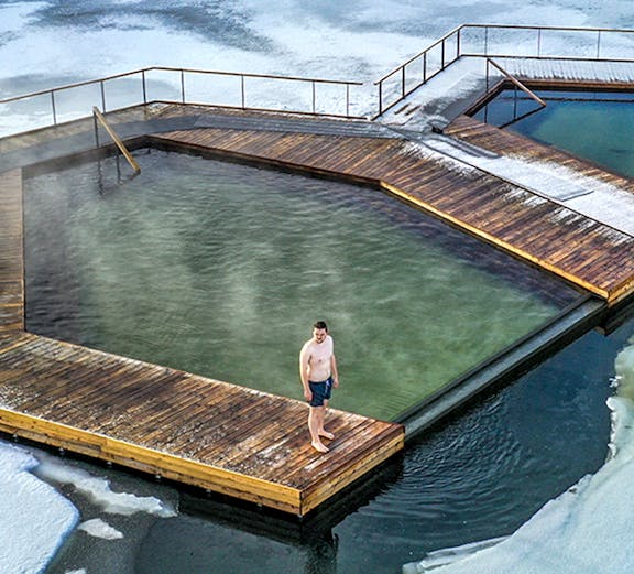 Guest standing on wooden deck at Vok Baths, surrounded by icy water in Iceland.