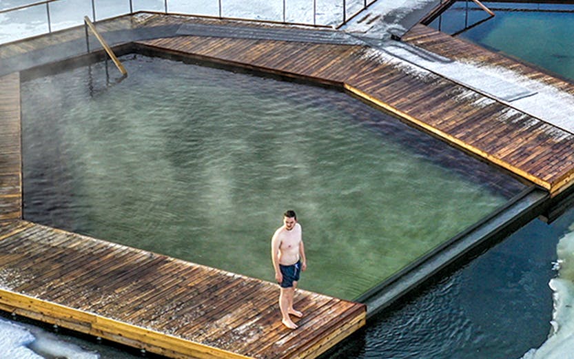Guest standing on wooden deck at Vok Baths, surrounded by icy water in Iceland.
