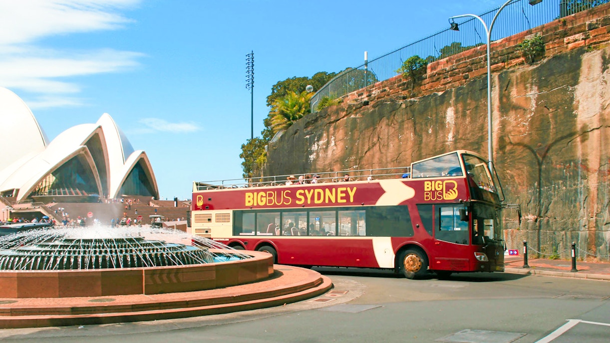 Sydney Hop-On-Hop-Off bus passing Sydney Opera House and Harbour Bridge.
