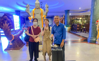 Travelers with luggage at Siem Reap Angkor Airport transfer service, standing by a statue.