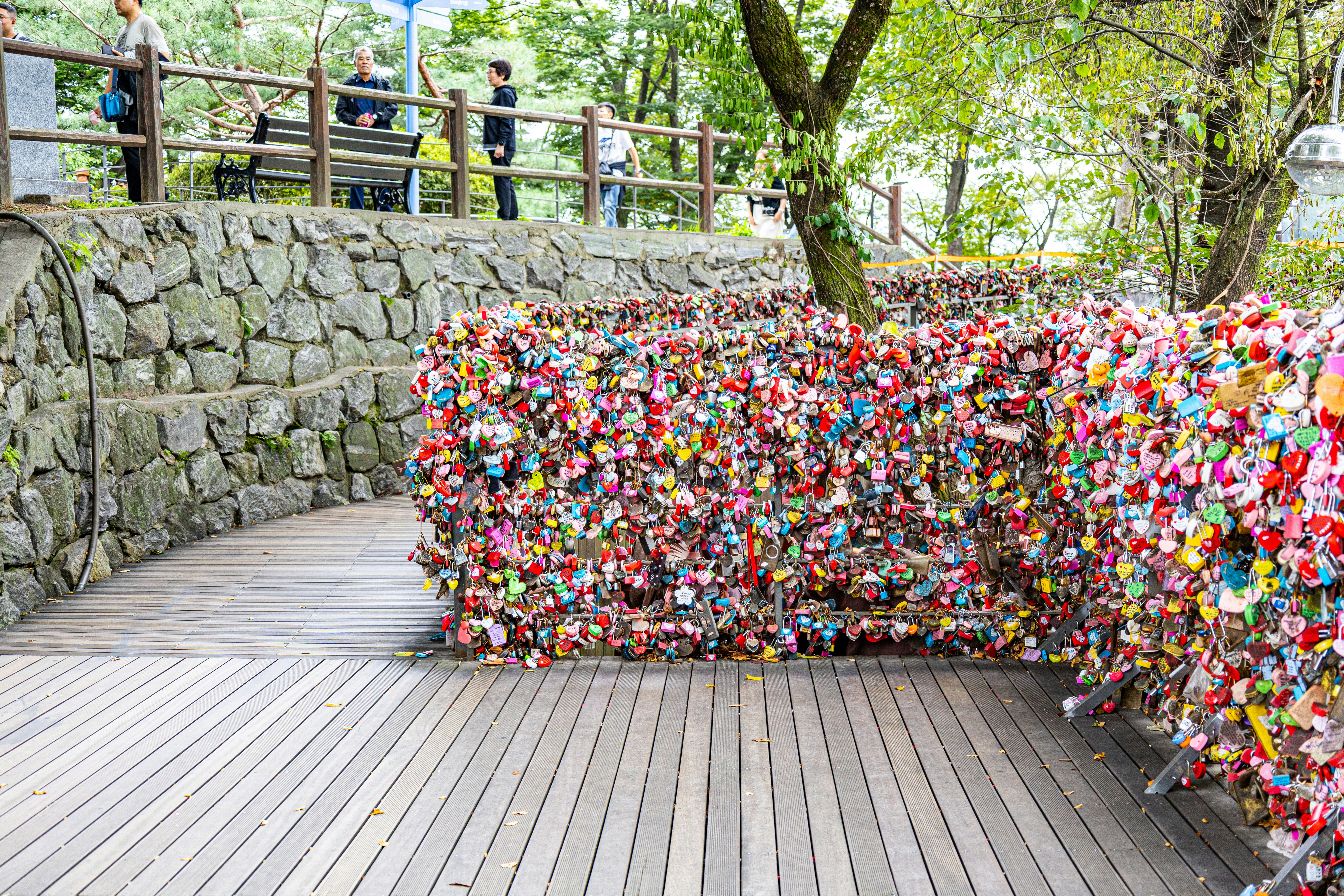 Love locks at N Seoul Tower in Seoul, South Korea, on a wooden walkway with stone wall and trees.