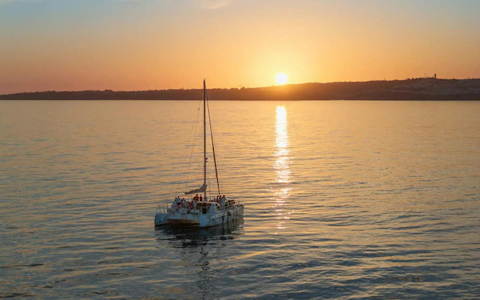 Catamaran sailing during Algarve sunset with passengers enjoying drinks.