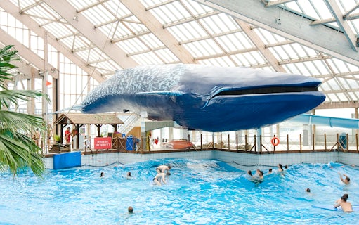 Indoor wave pool with swimmers under a large whale model at Aquaboulevard de Paris.