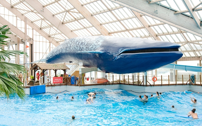 Indoor wave pool with swimmers under a large whale model at Aquaboulevard de Paris.
