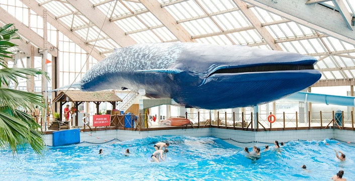 Indoor wave pool with swimmers under a large whale model at Aquaboulevard de Paris.