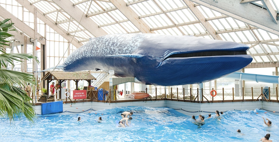 Indoor wave pool with swimmers under a large whale model at Aquaboulevard de Paris.
