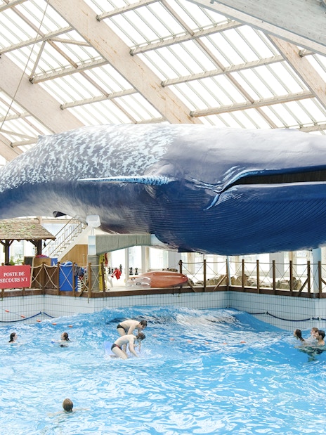 Indoor wave pool with swimmers under a large whale model at Aquaboulevard de Paris.