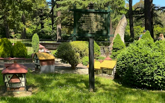 Miniature Tudor village in Fitzroy Gardens, Melbourne, surrounded by lush greenery and informational sign.