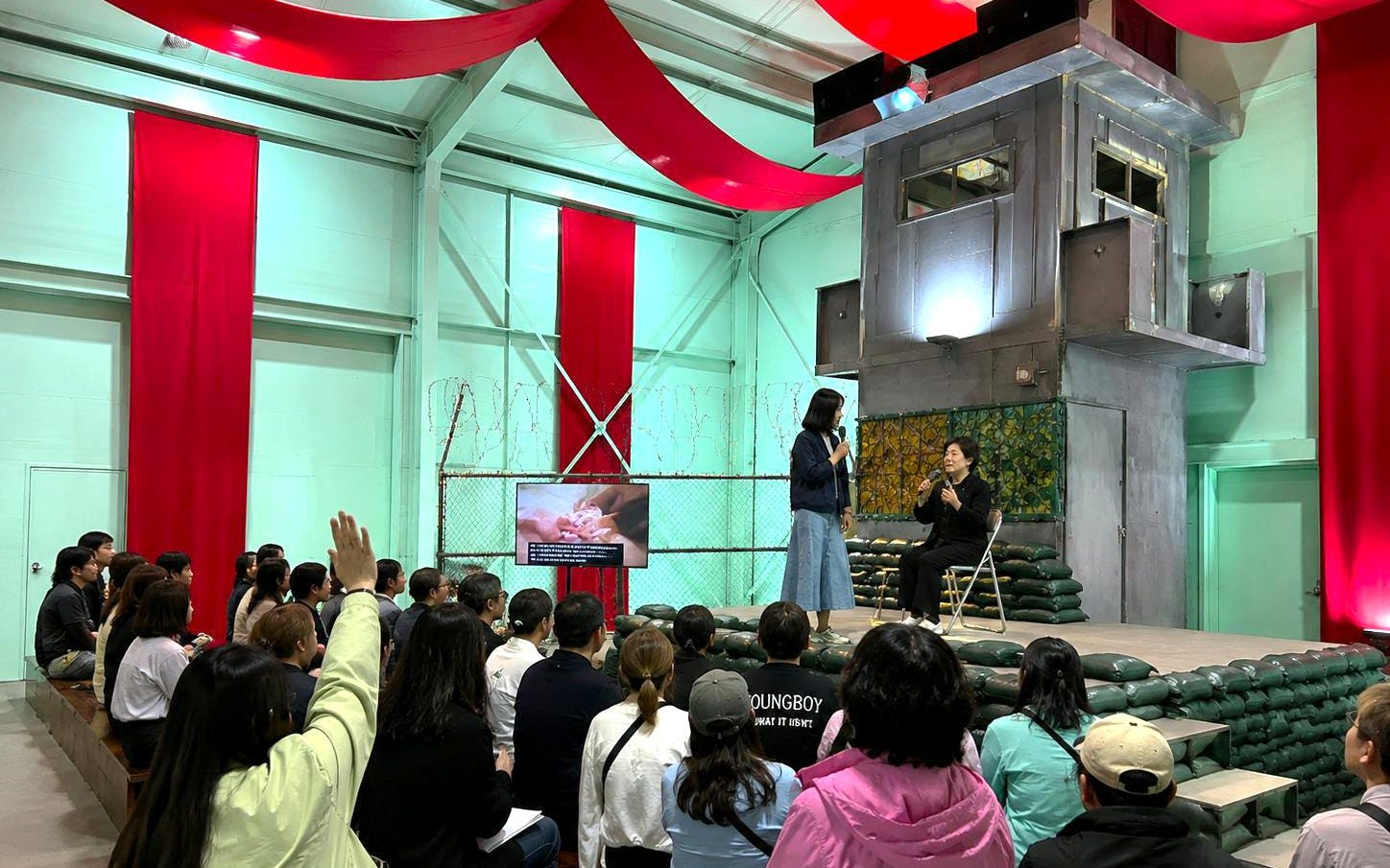 Audience at North Korea Experience Center 2 watching a presentation with speakers on stage.