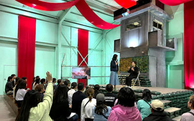 Audience at North Korea Experience Center 2 watching a presentation with speakers on stage.
