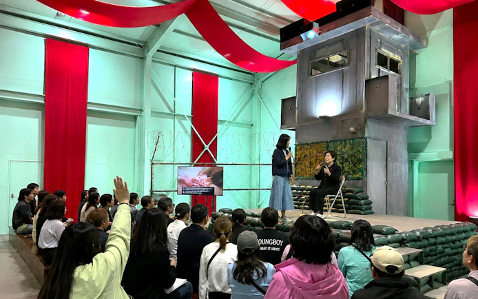 Audience at North Korea Experience Center 2 watching a presentation with speakers on stage.