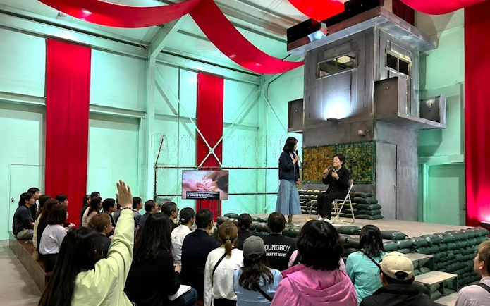 Audience at North Korea Experience Center 2 watching a presentation with speakers on stage.