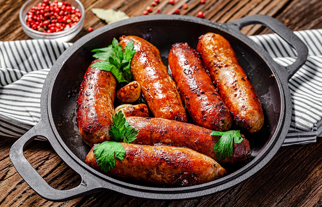 Pork sausages garnished with herbs in a skillet at Castas e Pratos, Douro Valley.