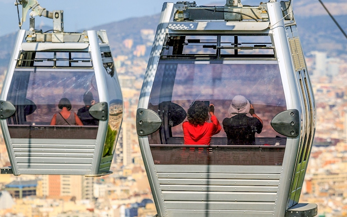 Montjuic cable cars with passengers overlooking Barcelona cityscape.